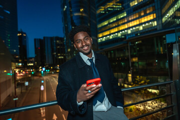 Young businessman holding smartphone smiling at night city