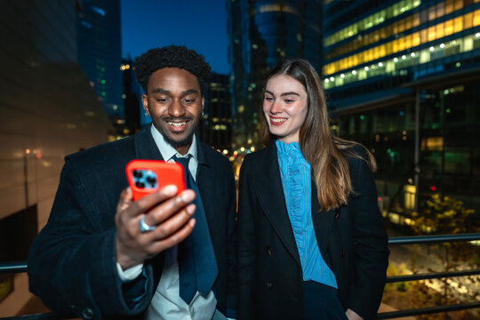 Business colleagues sharing content on smartphone in city at night