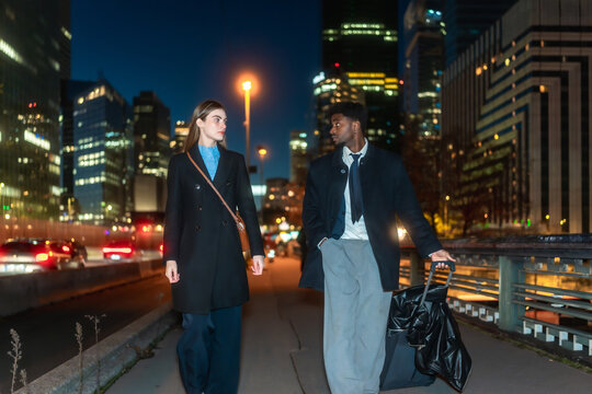 Professional man and woman walking city street at night - Powered by Adobe