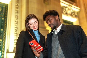 Diverse couple sharing phone screen in city night
