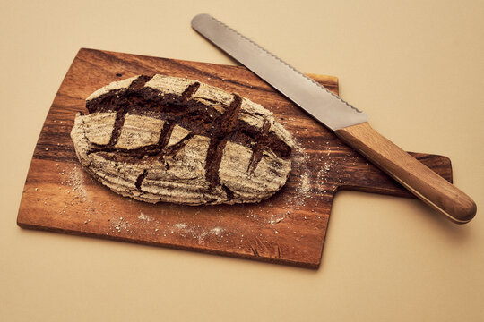 Still life shot of rustic brown rye bread loaf on cutting board with serrated knife
