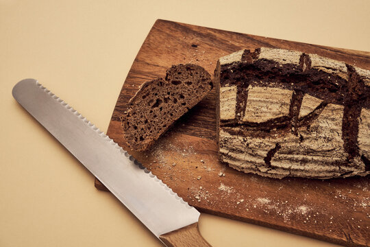 High angle still life of sliced, homemade rustic rye bread on cutting board with serrated knife
