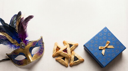 Purim holiday greeting card with carnival mask, blue gift box with gold Stars of David pattern and hamentashen cookies top view with space for text