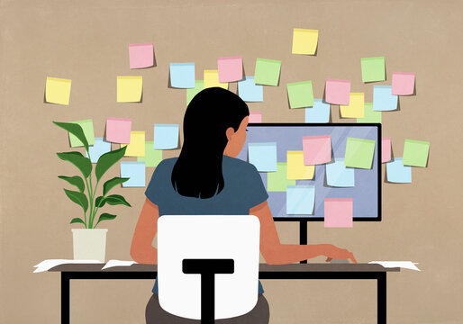 Sticky notes covering computer and wall in front of businesswoman working at desk

