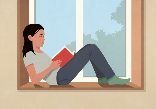 Woman reading book on sunny window ledge at home
