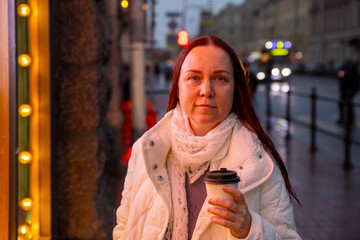 Obraz premium middle aged Caucasian woman drinks coffee in rain under neon lights. woman is walking alone in the city.