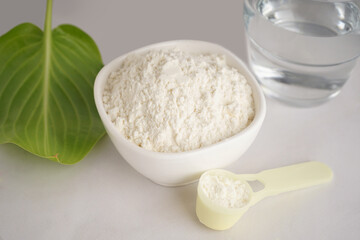 Scoop and bowl with collagen powder and glass of water on white background