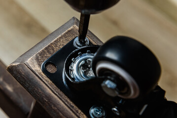 Screwing furniture wheels with brakes to a wooden table with a screwdriver.