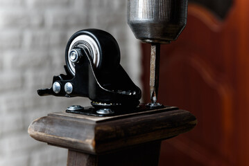 Screwing furniture wheels with brakes to a wooden table with a screwdriver.