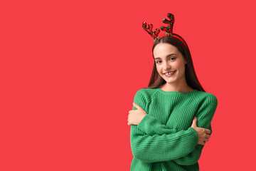 Young woman in sweater with Christmas reindeer horns on red background