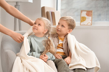 Obraz premium Mom giving plaid to her children on armchair at home
