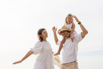 Cheerful family enjoying time together at the beach, with daughter on father shoulders and mother smiling beside, symbolizing love, bonding, parenthood and joyful summer vacation lifestyle.