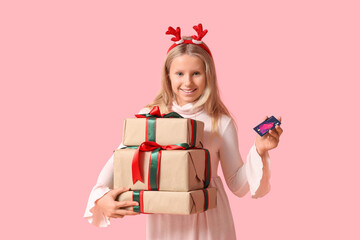 Cute girl in reindeer horns with credit card and gift boxes on pink background. Christmas celebration