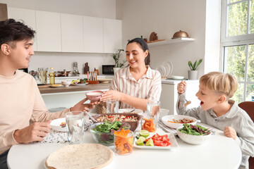 Parents with their little son eating tasty Fajita at table in kitchen