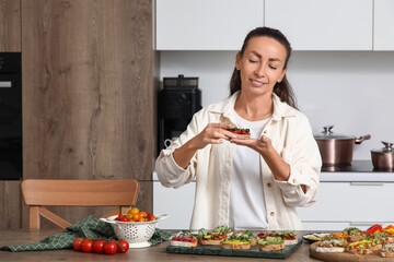 Beautiful woman with tasty vegan bruschettas at table in kitchen