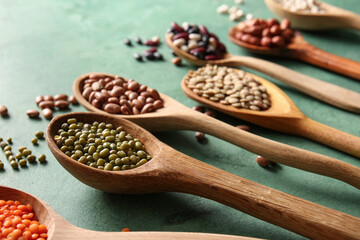 Composition with wooden spoons of different legumes on green background, closeup