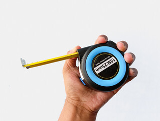 A close-up shot of a hand holding a retractable metal measuring tape against a clean white-gray background. Ideal for product showcases, tool catalogs, and construction-themed visuals.