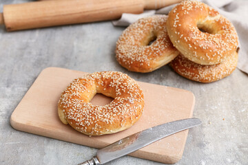 Wooden board of tasty bagels with sesame seeds on grey background, closeup