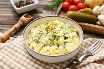Bowl of tasty potato salad with dill and vegetables on wooden background