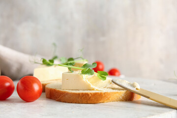 White wooden board of bread slices with triangles of tasty processed cheese and micro green on grey background