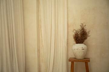 A cozy corner features a vase filled with dried flowers on a stool
