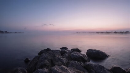 Obraz premium Calm waters at dusk with rocks in the foreground.