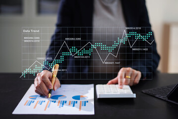 Hand using a stylus on tablet with digital trend graph overlay and laptop. Ideal for fintech, analytics, report, chart