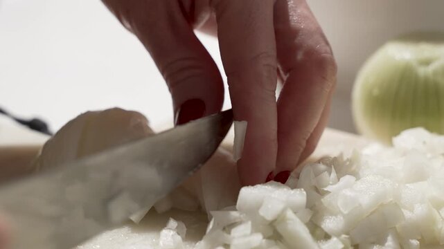 Close-up of a cook chopping white onion with a sharp knife on a cutting board. Fresh diced onions for cooking, shallow depth of field.