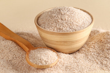 Bowl and spoon with psyllium husk powder on beige background, closeup