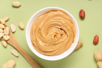 Bowl of tasty peanut butter with wooden spoon and nuts on green background