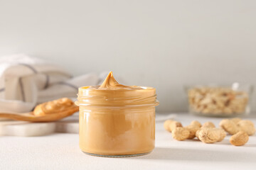 Jar of tasty peanut butter with nuts on white background