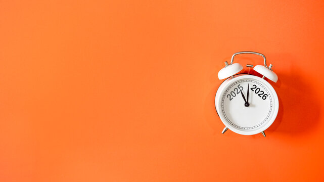 2025 and 2026 on black alarm clock on orange background, Merry Christmas and Happy new year concept. Copy space and banner for text