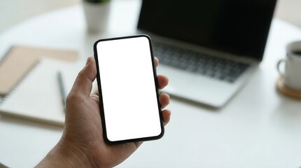 Hand Holding Modern Smartphone with Blank White Screen on Office Desk with Laptop