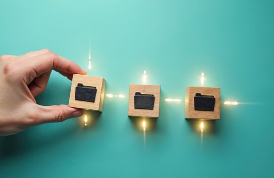Hand adds wooden block with folder icon to line of digital data storage. Organization of information, cloud sync, archiving concepts visually represented by connected cubes. File management workflow.