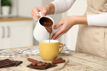 Woman pouring melted chocolate into cup on table in kitchen. Closeup