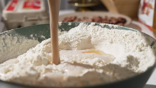 Liquid is poured into a flour well with an egg yolk in the center. Baking ingredients combine for fresh dough in close-up.