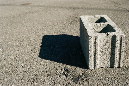 Concrete Block's Shadows: A close-up shot of a single, weathered concrete block casting a dramatic shadow on a rough asphalt surface, showcasing texture, form, and light.