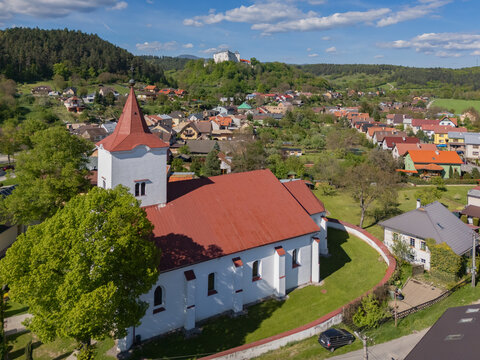 Aerial view of the Parish Church of Holy Trinity with its striking red roof and white walls standing out against the green landscape, Slovenska Lupca, Banska Bystrica Region, Slovakia.
