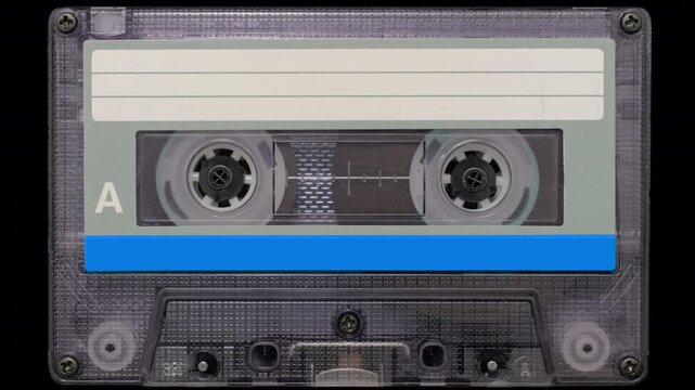 Vintage Audio Cassette Reels Spinning. Retro compact cassette tape with spinning reels on black background.	

