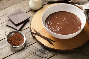 Bowl with hot chocolate, jar of milk and cocoa in sieve on wooden background. Closeup