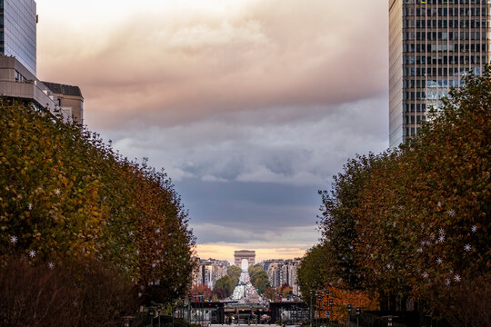 A picturesque autumn lane lined with trees leads the eye towards a distant Triumph Arch, capturing the beauty of seasonal change in an urban landscape.