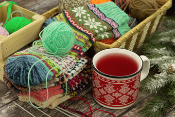 Colorful knitted socks, knitting yarn, hot tea, and a spruce branch create a wintery mood. Creating a cozy winter mood. Winter clothing.