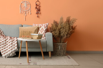 Comfortable sofa, table and vase with pampas grass near coral wall in living room