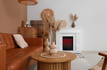 Fototapeta premium Interior of stylish living room with brown sofa, fireplace and pampas grass on coffee table