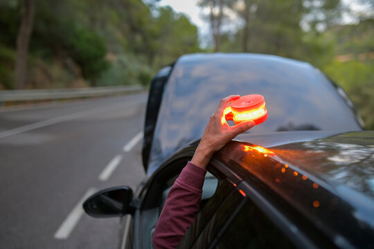 Hand placing V16 emergency safety beacon on a broken down car by roadside, indicating vehicle breakdown
