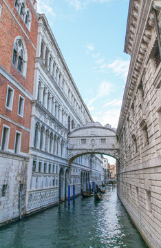 View of the Bridge of Sighs, connecting prison to Doge's Palace, spans over a narrow canal with gondolas gliding on the water, Venice, Veneto, Italy.