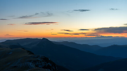 A breathtaking mountain range silhouetted against a vibrant sunset sky with hues of orange and blue
