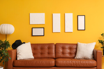 Brown leather sofa with soft pillows and floor lamp near yellow wall in living room
