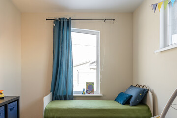 a cozy children's bedroom with a bed, a green bedspread, and a bedside table. There are blue curtains on the window.
