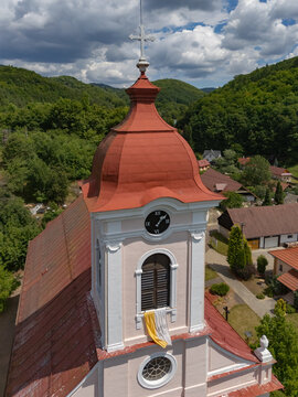 Aerial view of the Church of St. Luke, its steeple adorned with a cross, stands majestically against the backdrop of verdant hills, Sklene Teplice, Banska Bystrica Region, Slovakia.